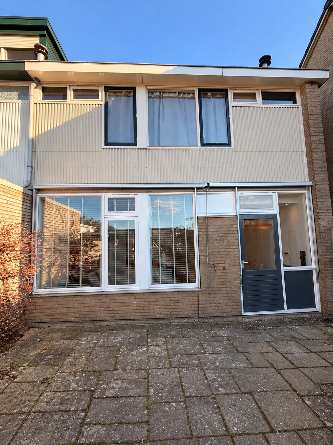 Voor: lichte houten gevelbekleding en oude houten kozijnen van dezelfde woning